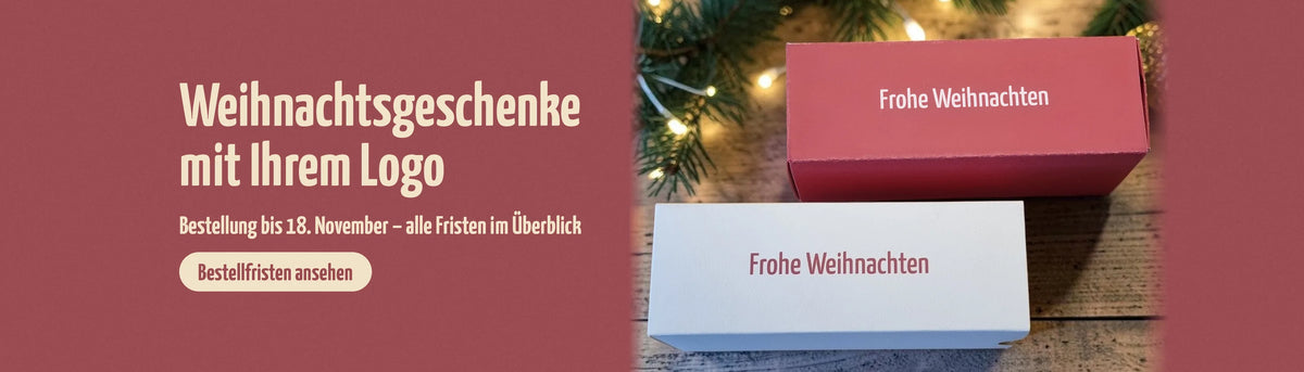 Zwei Geschenkboxen mit der Aufschrift „Frohe Weihnachten", eine in Rot und eine in Weiß, vor Tannenzweigen und Lichterkette